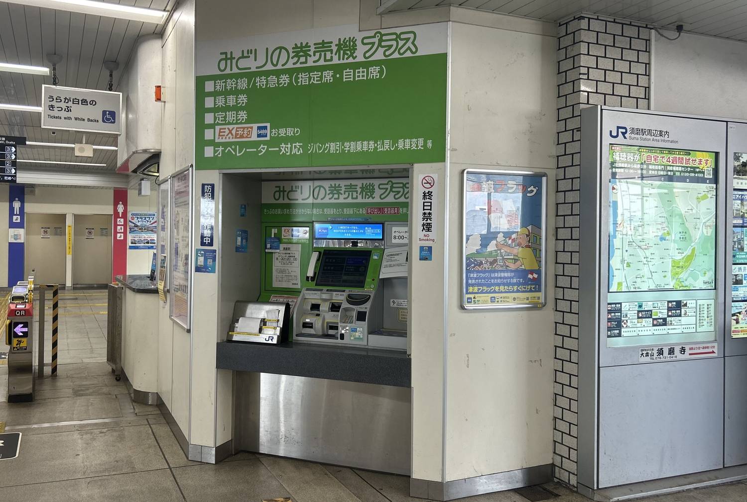 A ticket machine bay inside a JR station: a green wall panel headed Midori no Kenbaiki Plus lists Shinkansen and limited express tickets with reserved and non-reserved seats, ordinary tickets, commuter passes, EX reservation collection and operator assistance; a green-cased touchscreen machine stands in the recess, with a station area map board to the right