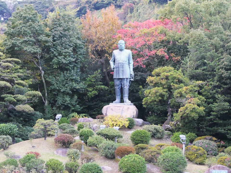 鹿兒島市城山町的西郷隆盛銅像,穿軍服的立像站在大石台座上,四周是修剪成球狀的灌木與轉紅的樹