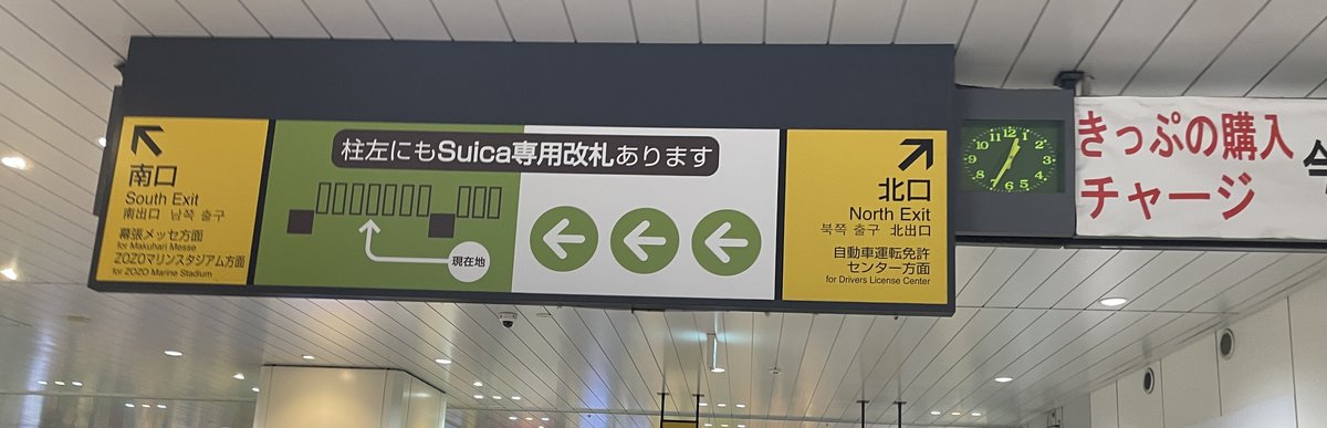 海浜幕張站剪票口內的黃色指示牌:左邊「南口 South Exit」下方寫著「幕張メッセ方面」,右邊「北口 North Exit」寫著自動車運転免許センター方面,中間綠底寫著柱子左側也有 Suica 專用剪票口