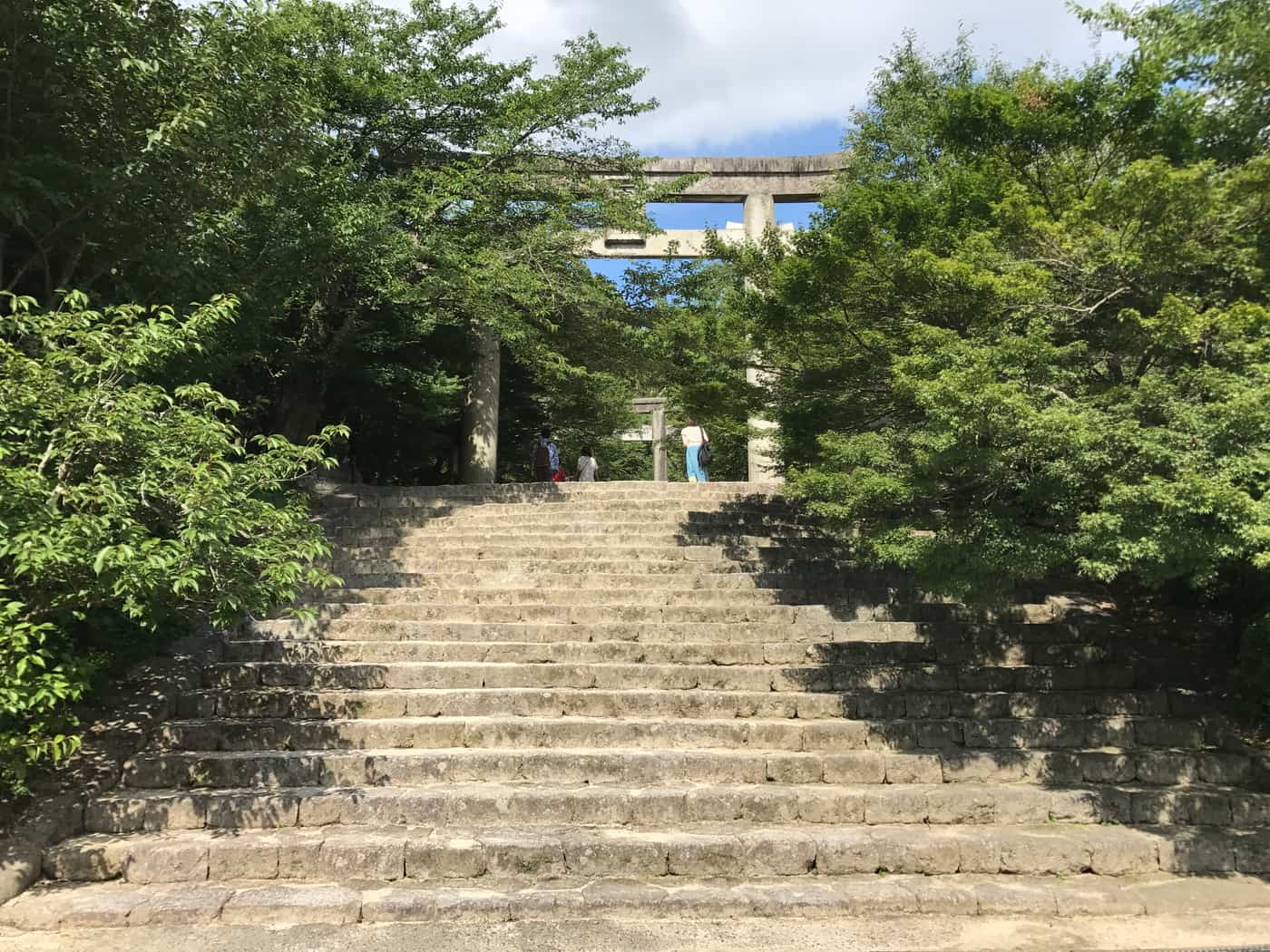 Torii gate and stone steps on the approach to Homangu Kamado Shrine, flanked by forest at the foot of Mount Homan