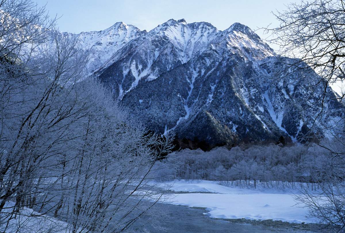 Snow-covered Kamikochi in winter with the Maehotaka ridge behind a half-frozen Azusa River and frost-coated trees