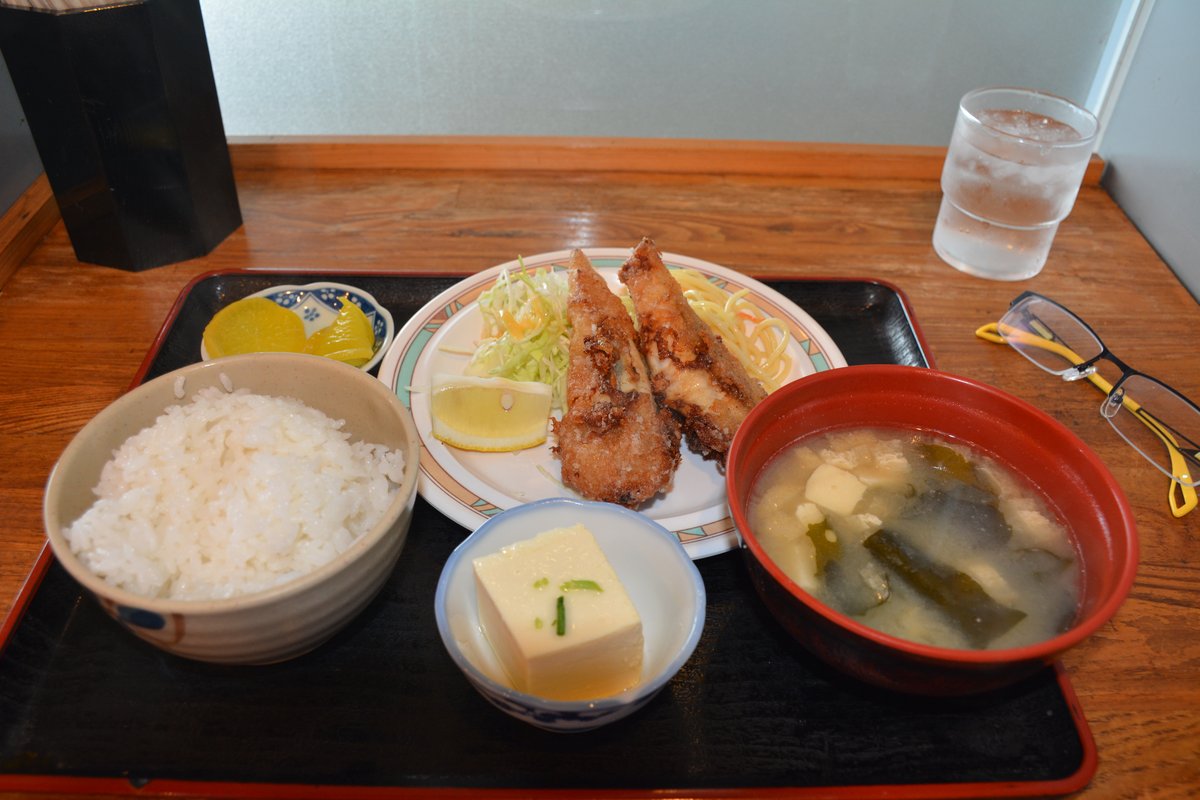 木桌上的托盤裡擺著一份河豚唐揚定食:兩塊炸河豚配高麗菜絲與檸檬、白飯、味噌湯、冷豆腐和醃黃蘿蔔