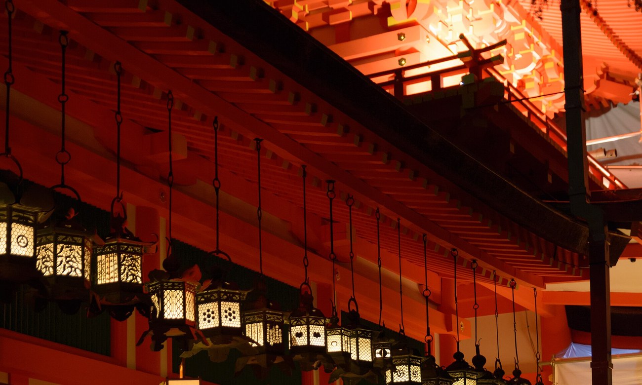 Kasuga Taisha corridor during the Setsubun Mantoro, rows of bronze hanging lanterns lit by candle flame against vermilion beams