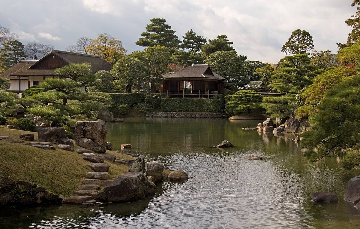 秋天的桂離宮池泉庭園：左前方草坡上一排飛石通到水邊，隔著池水是書院一帶的建築與修剪過的松樹