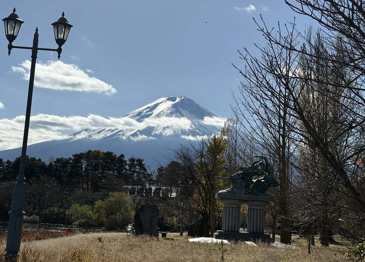 大池公園的枯草地、歐式雙頭路燈與石柱上的雕像,落葉的樹後方是山腰繞著雲、山頂積雪的富士山
