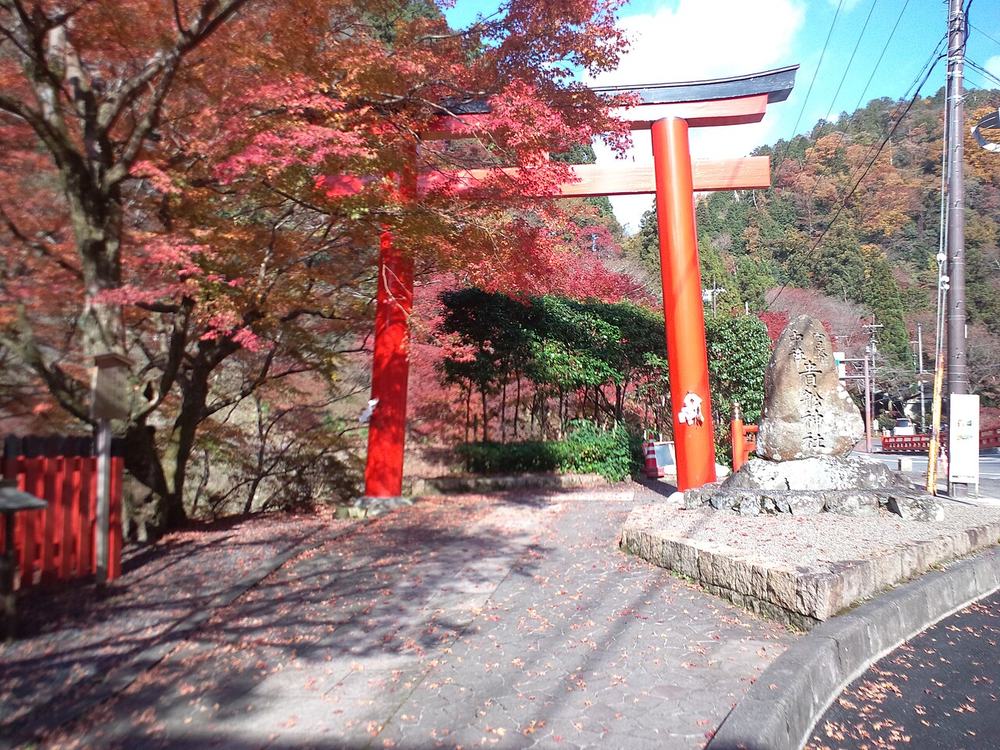 貴船神社的一之鳥居：朱紅色大鳥居立在車道轉彎處，右側一塊刻著「貴船神社」的石碑，左邊是整棵轉紅的楓樹，地上散著紅葉，遠處山坡也有紅葉