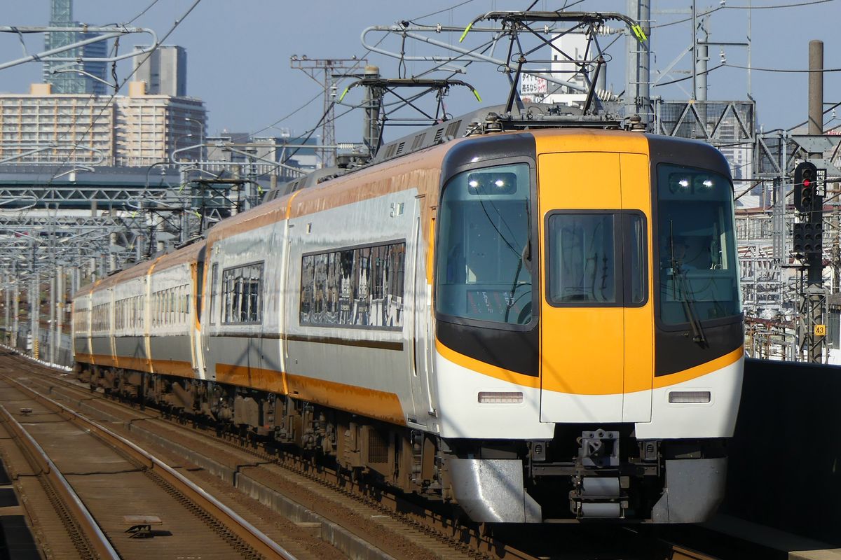 行駛在高架軌道上的近鐵特急列車：車頭是白底配黃色、車窗周圍深色的造型，後面連著好幾節車廂
