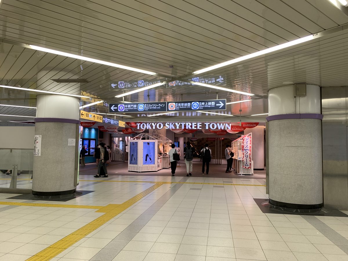 押上站地下的寬敞通道，正前方的入口上方寫著 TOKYO SKYTREE TOWN，天花板的指標分別指向半藏門線、晴空塔線、淺草線與押上線，地上有黃色導盲磚