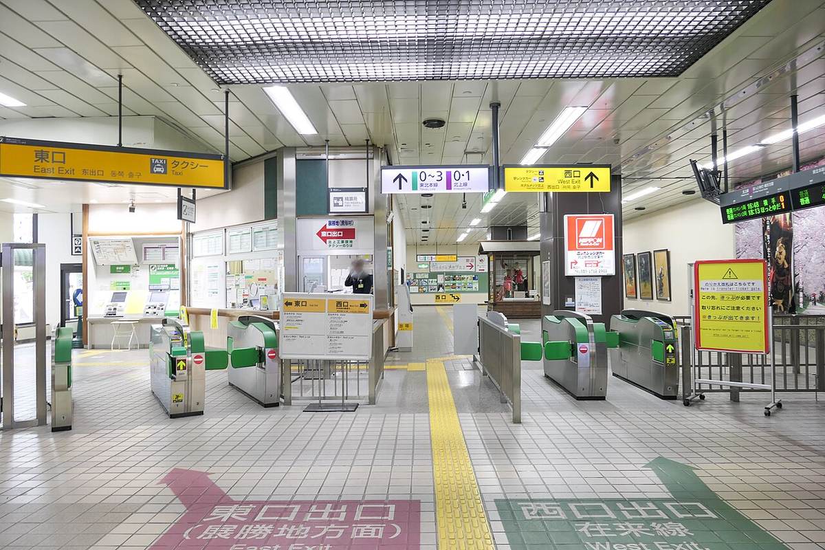 JR 北上站站內的改札口：左上方黃色吊牌寫「東口 East Exit／タクシー」，地板左側有粉紅色箭頭寫「東口出口（展勝地方面）」，右側綠色箭頭寫「西口出口 在来線」，中間是綠色的自動改札機