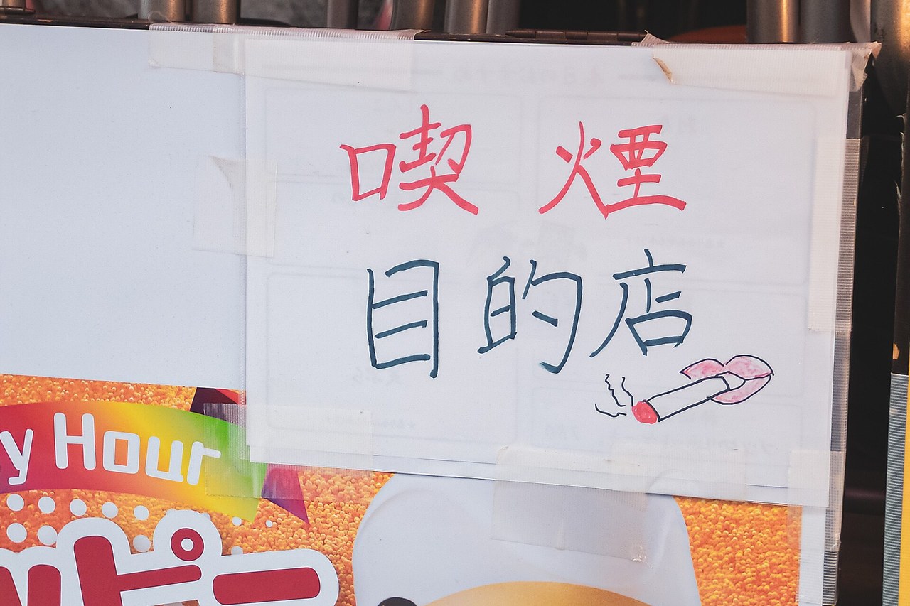 A handwritten notice taped to a shopfront in Kanda reading kitsuen mokutekiten in red and black marker beside a drawing of a lit cigarette