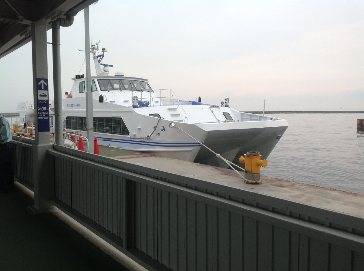 關西機場高速船碼頭:白色雙體高速船「うみ UMI」靠在碼頭邊,船身寫著神戸-関空ベイシャトル,左邊柱子上的藍色牌子寫「GATE2 神戸行 For Kobe」