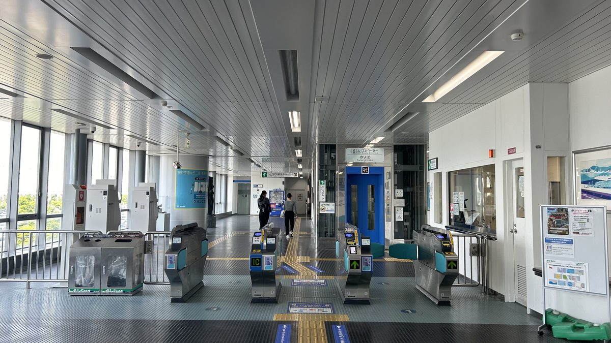 Port Liner 神戸空港站的改札口:一排銀色自動閘門,最左邊那台標著「IC 専用」,閘門側面貼著 PiTaPa、ICOCA 標誌與綠色箭頭,後方是寫著「のりば」的藍色電梯,左邊落地窗外是綠樹