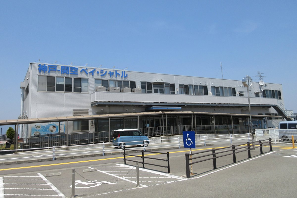 神戶機場的海上アクセスターミナル:兩層樓的白色建築,外牆上方是藍色大字「神戸-関空 ベイ・シャトル」,一樓有長長的遮雨棚,前方是停車場與無障礙車位標示