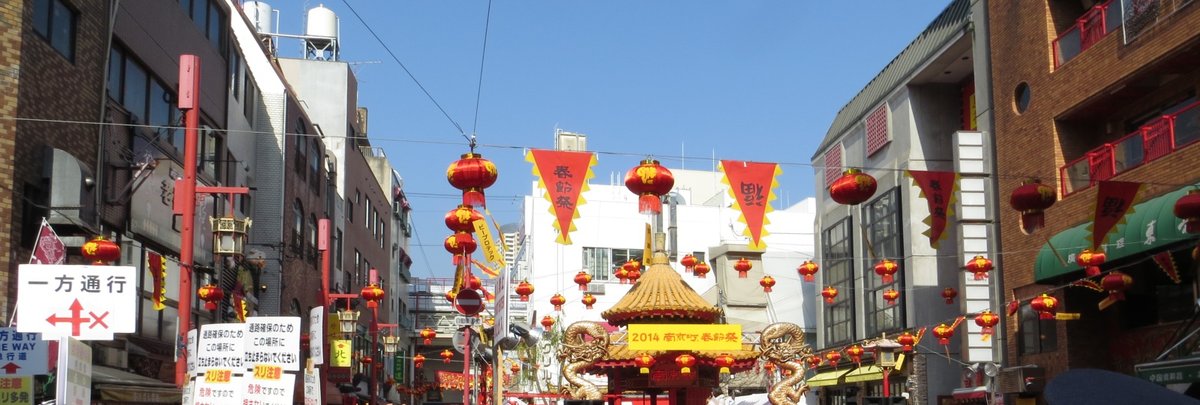 2014 年神戶南京町春節祭:街上掛滿紅燈籠與寫著春節祭的三角旗,廣場涼亭掛著「2014 南京町春節祭」黃色看板,左邊立著「一方通行」告示牌與提醒扒手、不要停留的看板