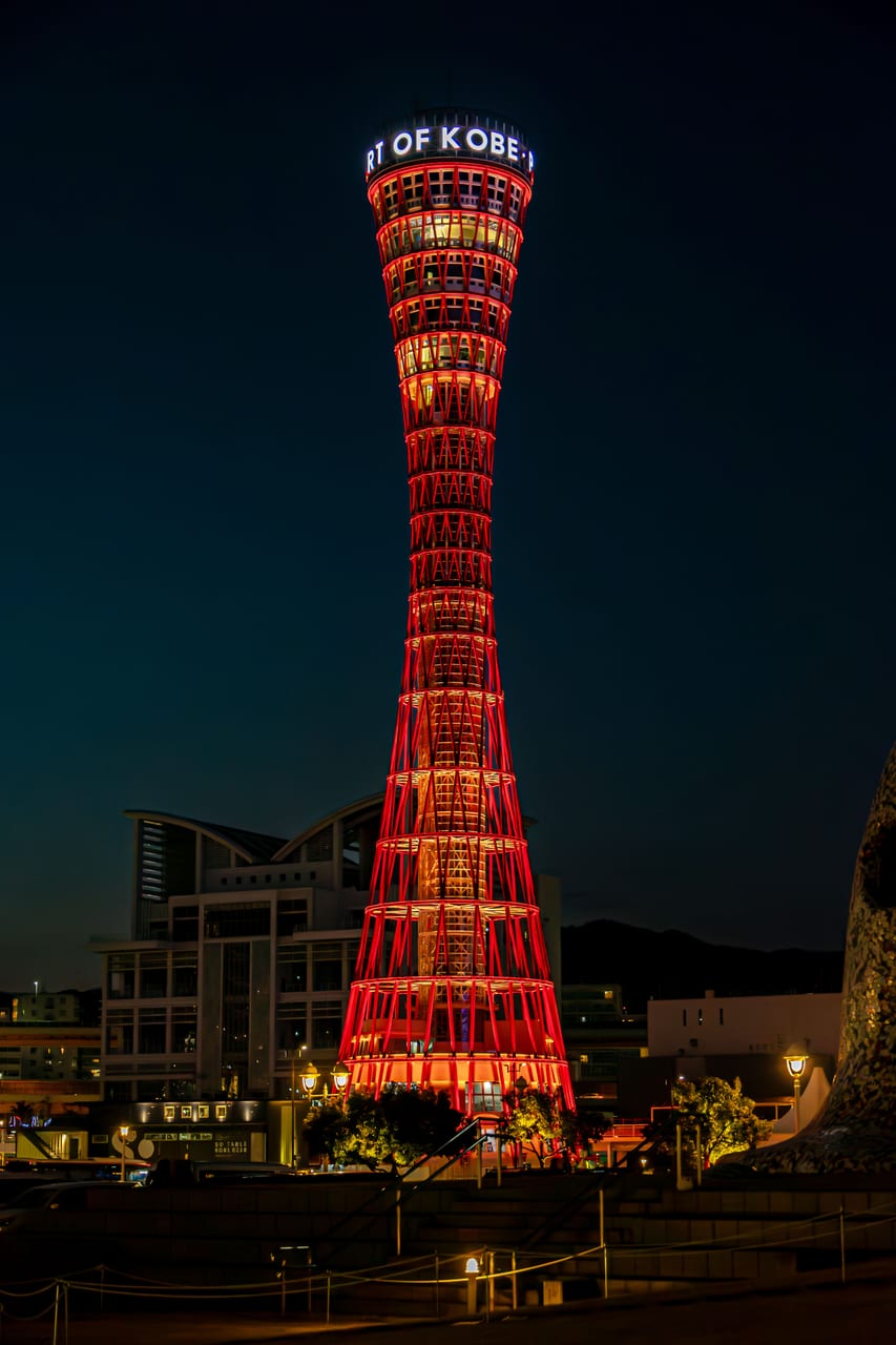 The red lattice tower of Kobe Port Tower beside the white net-roofed Maritime Museum