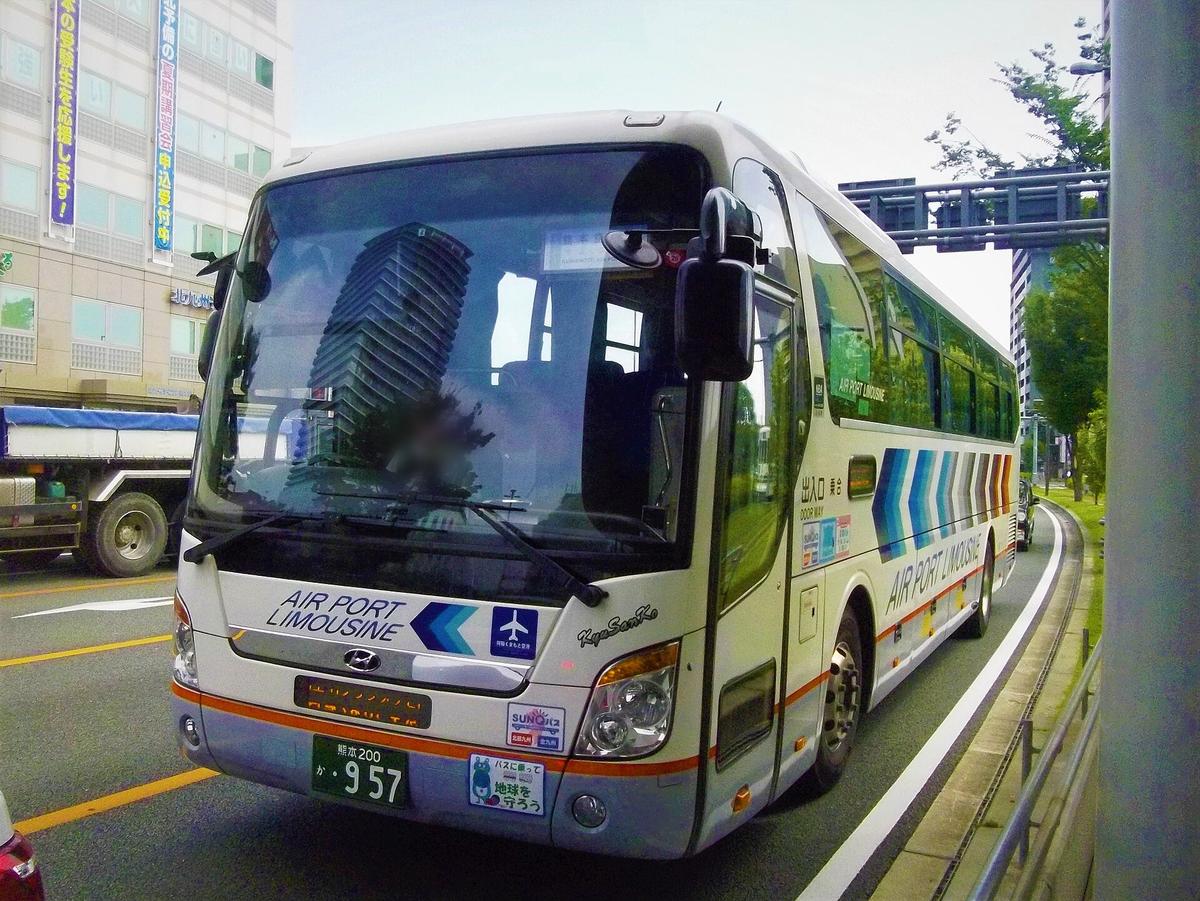 九州產交的機場利木津巴士:白色大型客運,車頭與車身側面印著藍色字「AIR PORT LIMOUSINE」和飛機圖示,車身有藍、灰、橘的斜條紋,停在市區大馬路邊
