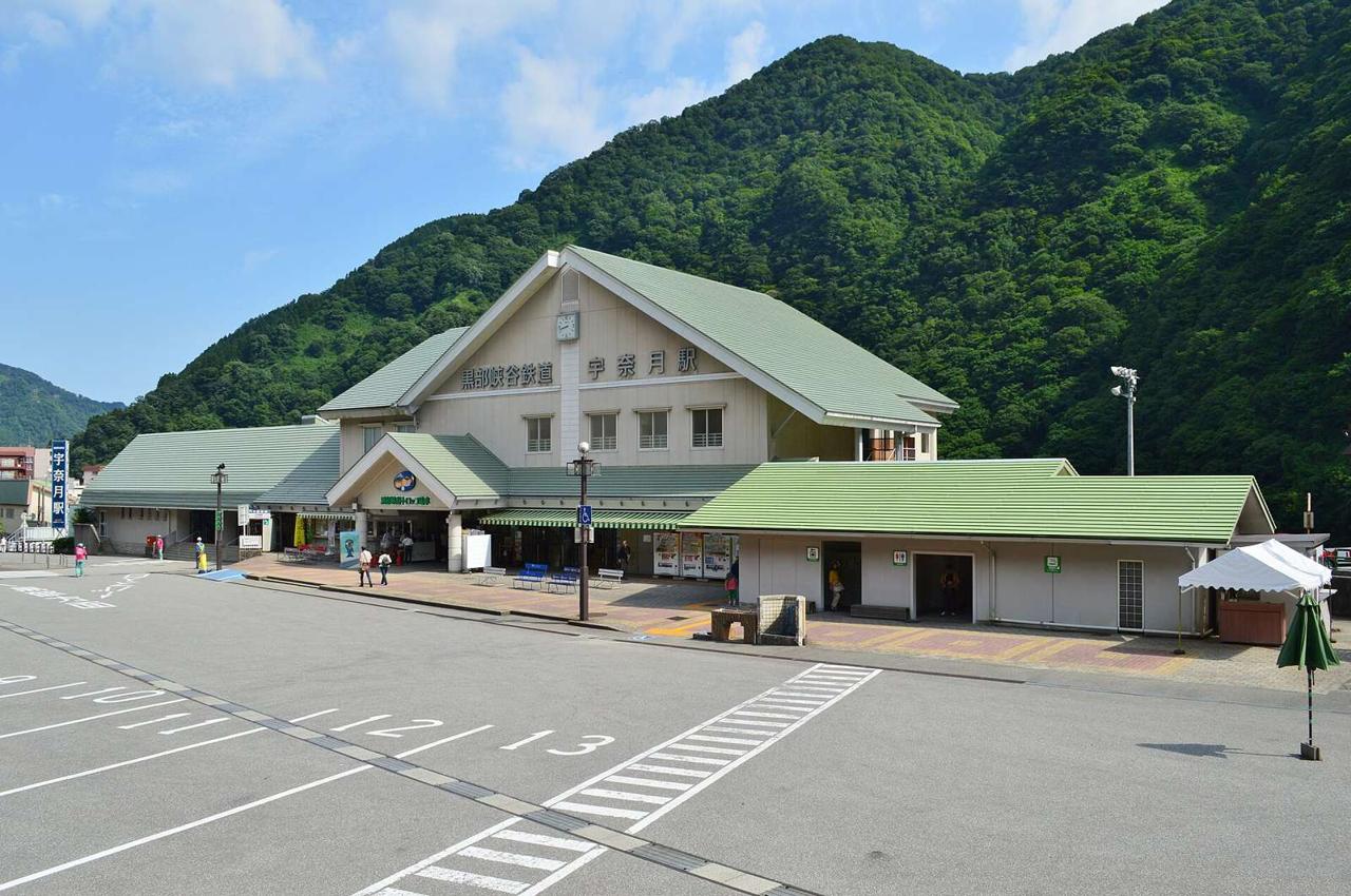 The Unazuki station building of the Kurobe Gorge Railway, a gabled hall with pale green tiled roofs and a clock, fronted by a wide empty coach park