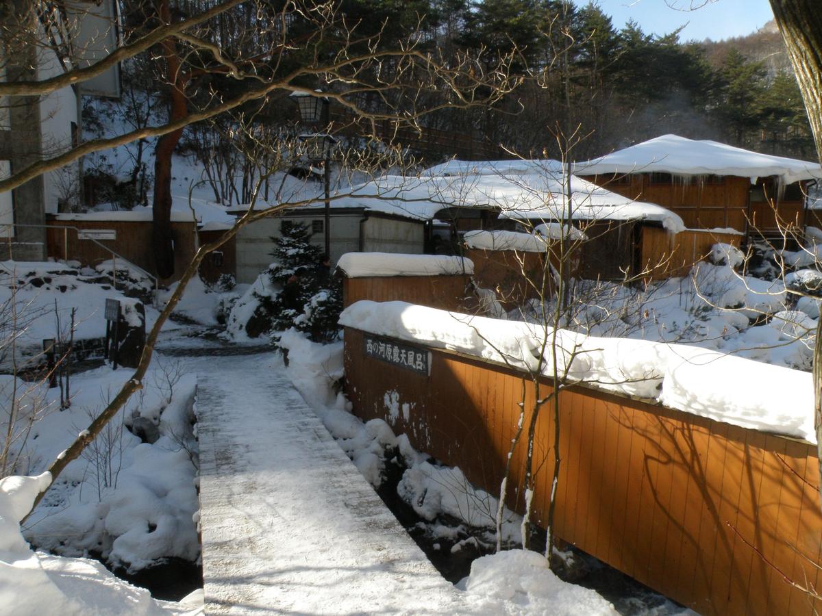 雪中的西の河原露天風呂,木板圍牆上掛著「西の河原露天風呂」名牌,前方是積雪的小橋
