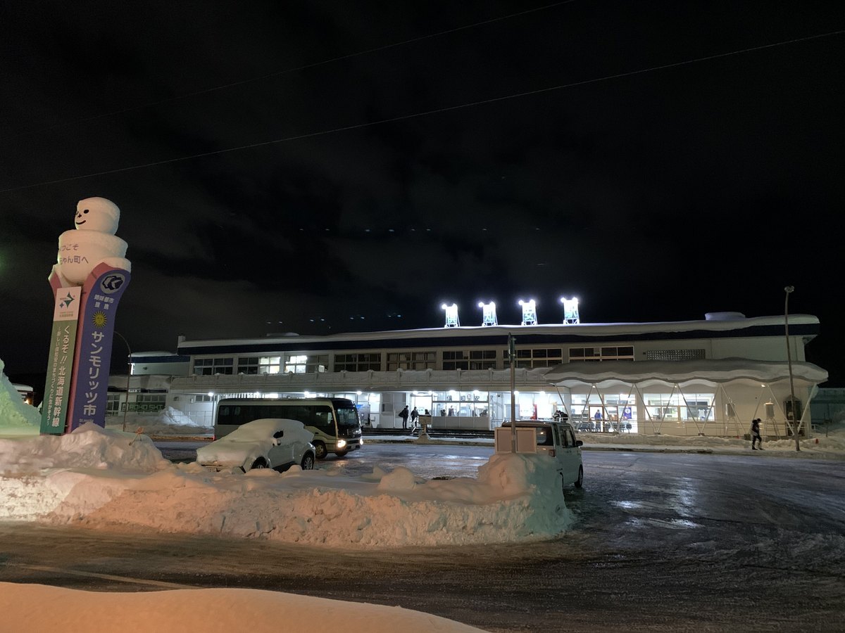A winter night outside Kutchan Station in Hokkaido: plowed snow banks stand taller than a person and a parked car sits almost completely buried