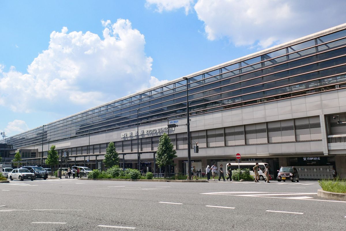 JR 京都站八條口一側的站房外觀:灰色石材與玻璃帷幕的長形建築,牆上有「JR 京都駅 KYOTO STATION」字樣,前方是車道與計程車
