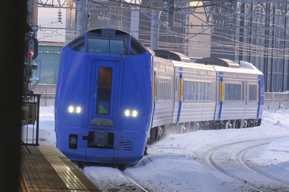 藍色車頭的 JR 北海道 キハ261 系特急列車開進積雪的札幌站,車頭寫著 SE-103,兩盞車頭燈亮著,鐵軌和月台邊堆滿白雪