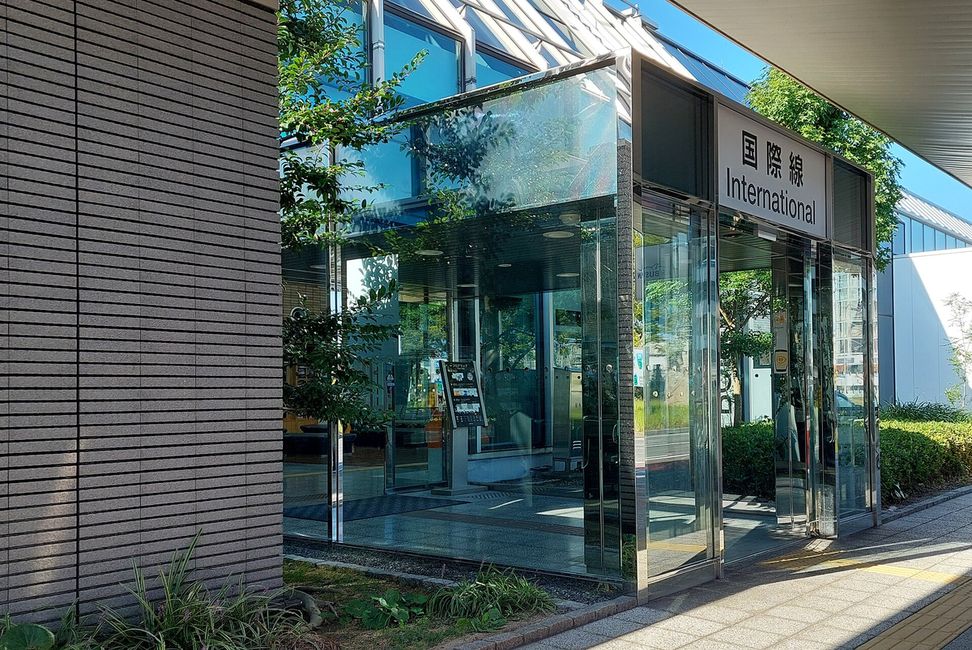 松山空港航廈的玻璃門入口,門上方掛著寫「国際線 International」的白色招牌,左邊是深灰色條紋外牆,玻璃後面看得到樹