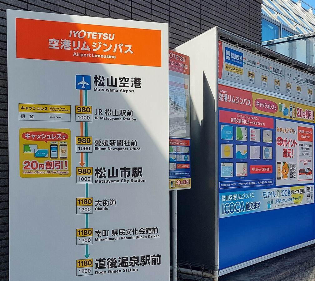 松山空港的伊予鐵「空港リムジンバス」路線看板:由上往下列出松山空港、JR松山駅前、愛媛新聞社前、松山市駅、大街道、南町県民文化会館前、道後温泉駅前,每站旁有兩個票價數字,愛媛新聞社前是 980 與 1000;右邊是 IC 卡與無現金支付的宣傳看板