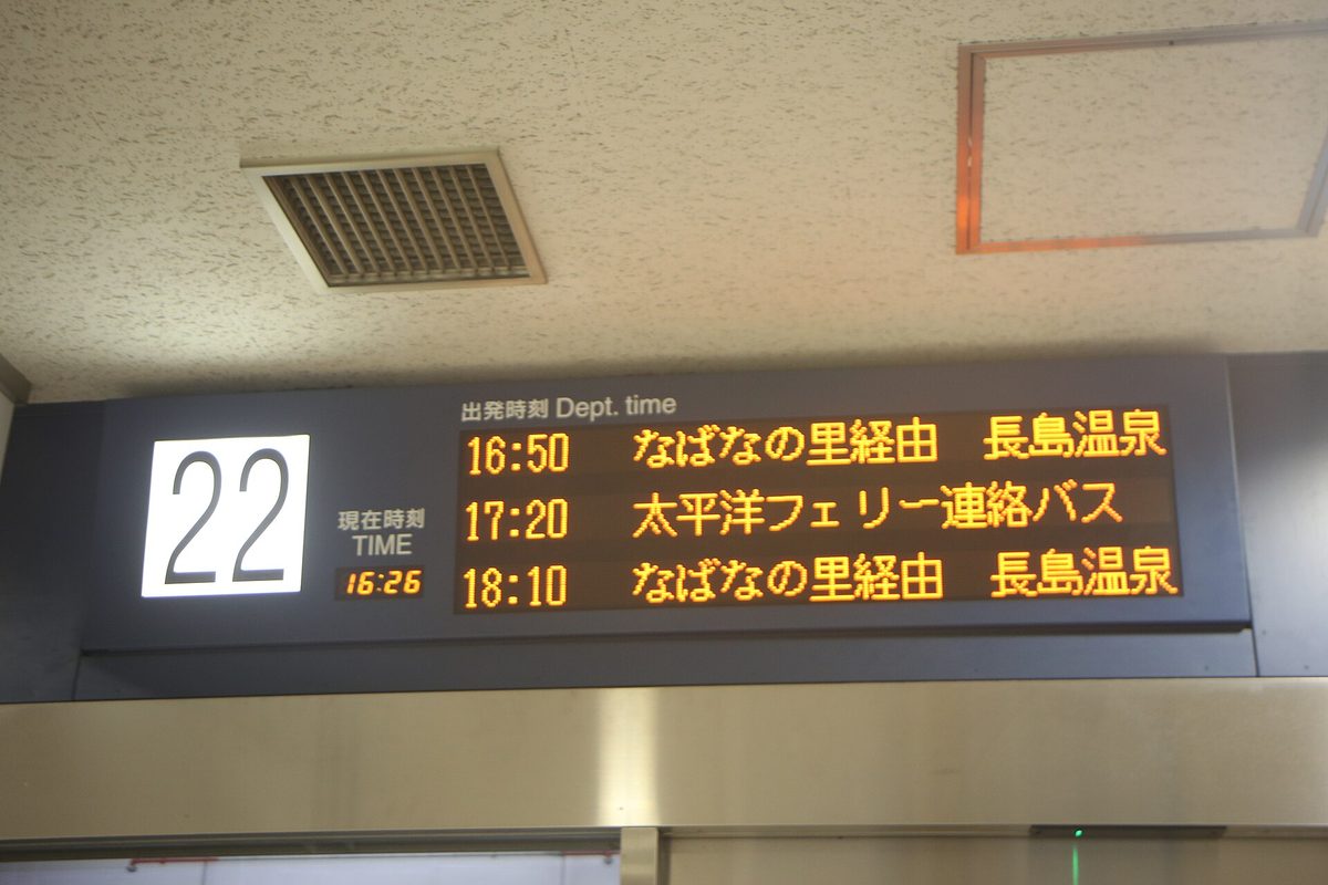 Departure board at platform 22 of Meitetsu Bus Center in orange LED text, three rows in Japanese: 16:50 via Nabana no Sato to Nagashima Onsen, 17:20 Taiheiyo Ferry shuttle, 18:10 via Nabana no Sato to Nagashima Onsen; the clock at left shows 16:26