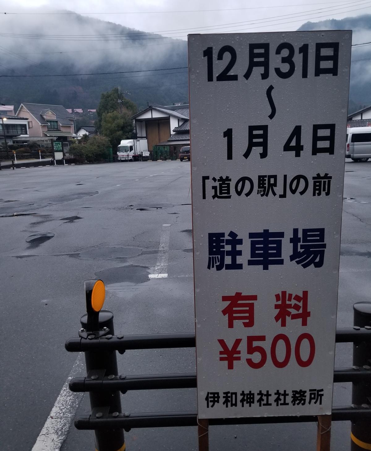 A hand-lettered standing notice board at the edge of a roadside-station car park in Hyogo, announcing that from 31 December to 4 January the lot in front of the michi-no-eki becomes paid parking at 500 yen, signed by the office of Iwa Shrine.