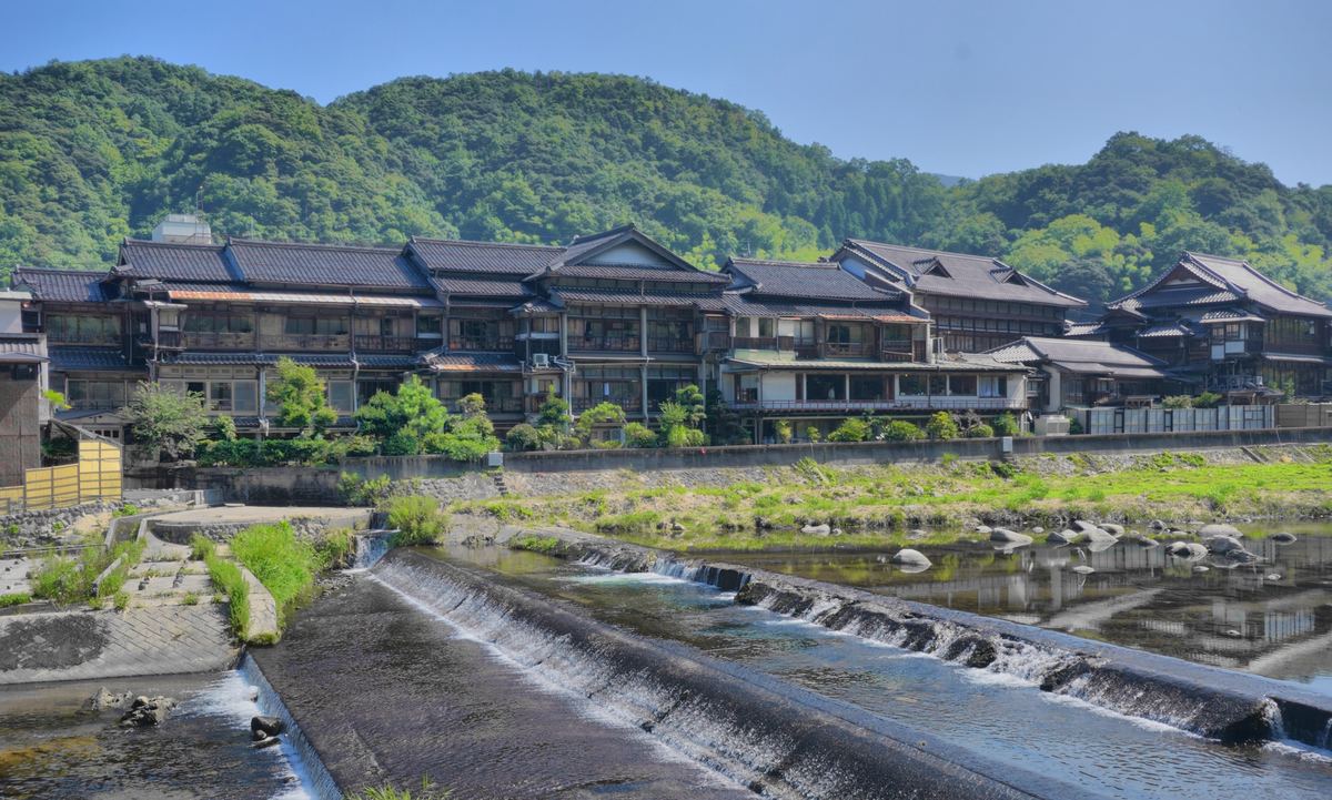 綠色山坡下,三朝溫泉沿三徳川一字排開的多層木造老旅館,前景是河上的低矮攔河堰與白色水花