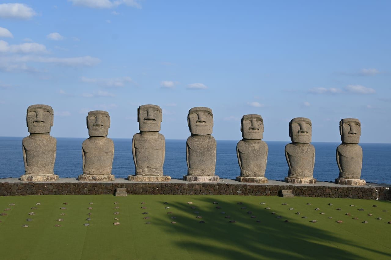 Seven full-size replica Moai with their backs to the hill on the hillside at Sun Messe Nichinan