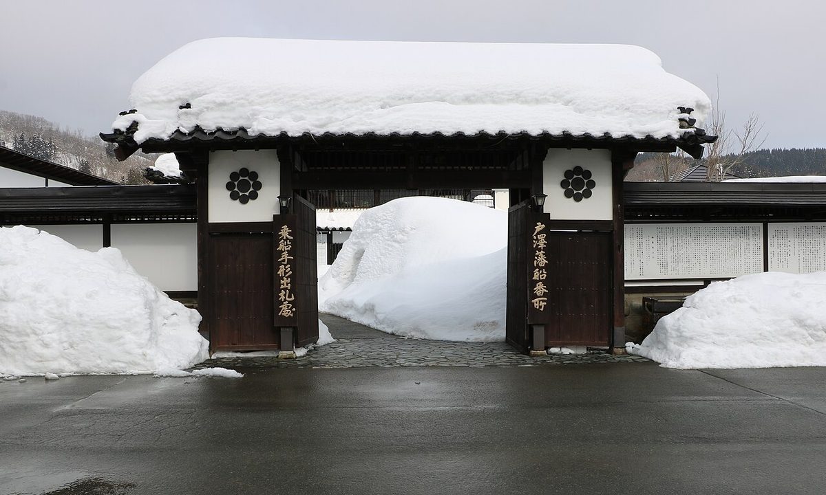 戶澤藩船番所的木造大門：瓦屋頂上積著厚雪，右門柱掛著「戶澤藩船番所」、左門柱掛著「乘船手形出札處」的木牌，門內與門外兩側都堆著比人高的雪堆