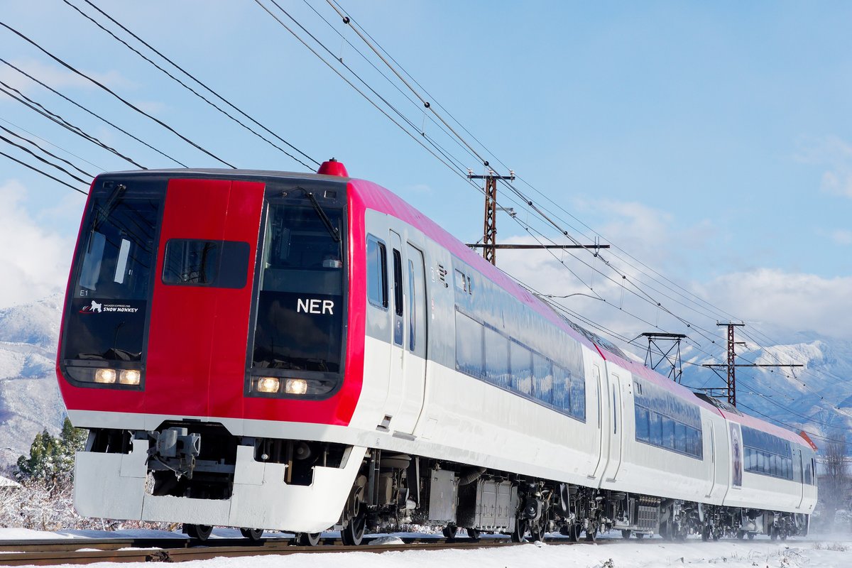 紅色車頭、白色車身的長野電鐵特急列車行駛在雪地鐵道上,背景是積雪的山