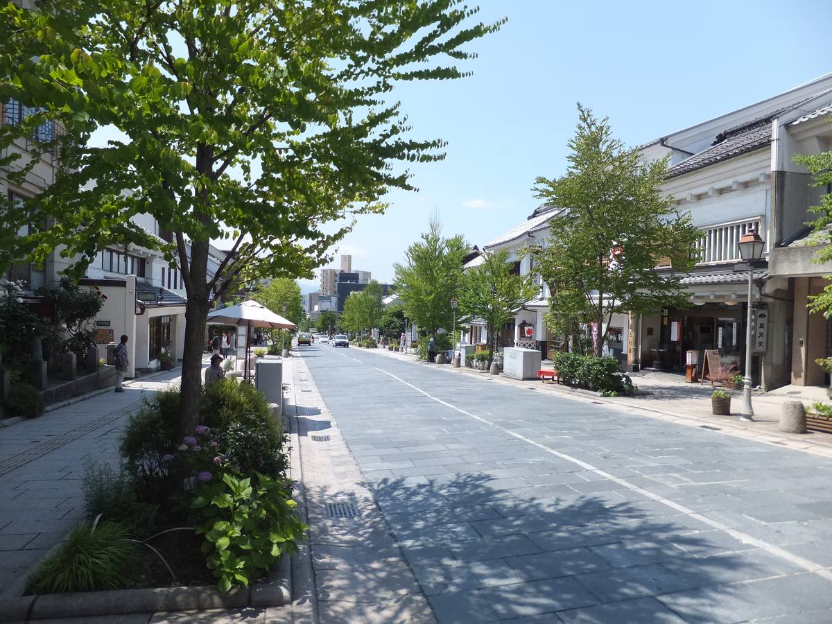 長野市中央通り的石板路段:灰藍色石板鋪成的車道筆直往下延伸,兩側是白牆黑瓦的倉造店家與行道樹,遠處是市區的高樓