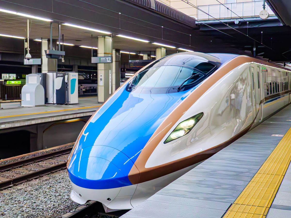 北陸新幹線 E7 系列車停在長野站月台:藍色車頭、白色車身配銅色飾帶,月台地上一條黃色導盲磚,左後方柱子上掛著 12 號月台的牌子