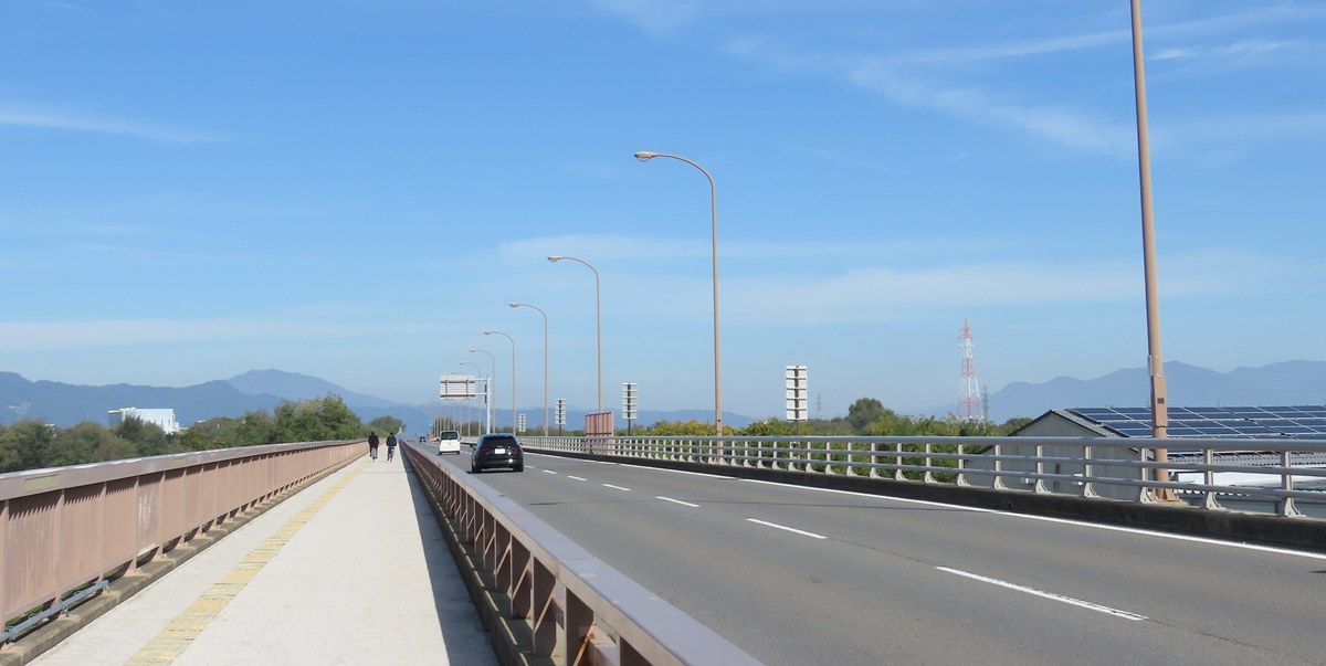 五輪大橋橋面:右邊是雙向車道與一排高路燈,左邊是有欄杆隔開的人行道,遠處是低矮的山稜