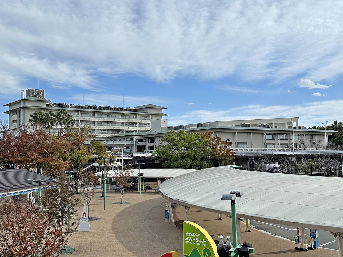 The Nagashima Onsen end: a cream multi-storey building with a rooftop sign reading Nagashima Onsen Yuami no Shima at back left, a plaza with white curved canopies and parked buses in front, and a green Nagashima Spa Land sign at bottom right, with autumn foliage