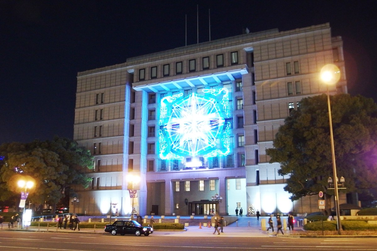 Osaka City Hall at night, a large illuminated motif mounted across the front of the building with the block floodlit in blue and white