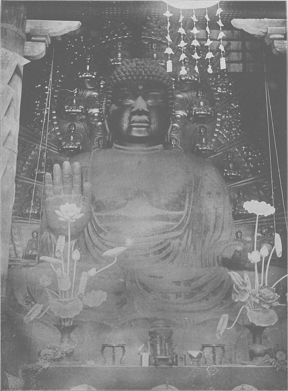 Meiji-era black-and-white photograph of the Great Buddha of Todaiji with lotus offerings before it