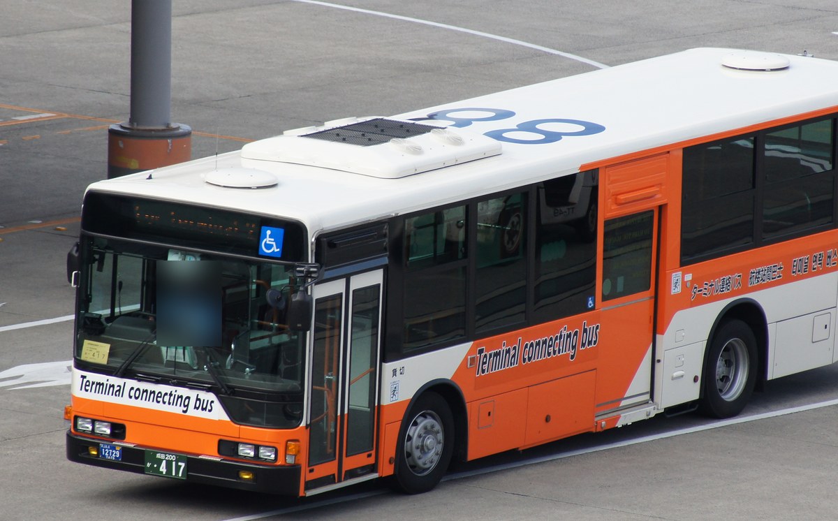 成田機場停機坪上一台橘白配色的低底盤巴士，車頭與車身寫著「Terminal connecting bus」，車側印有日文「ターミナル連絡バス」與中韓文字，車號 888