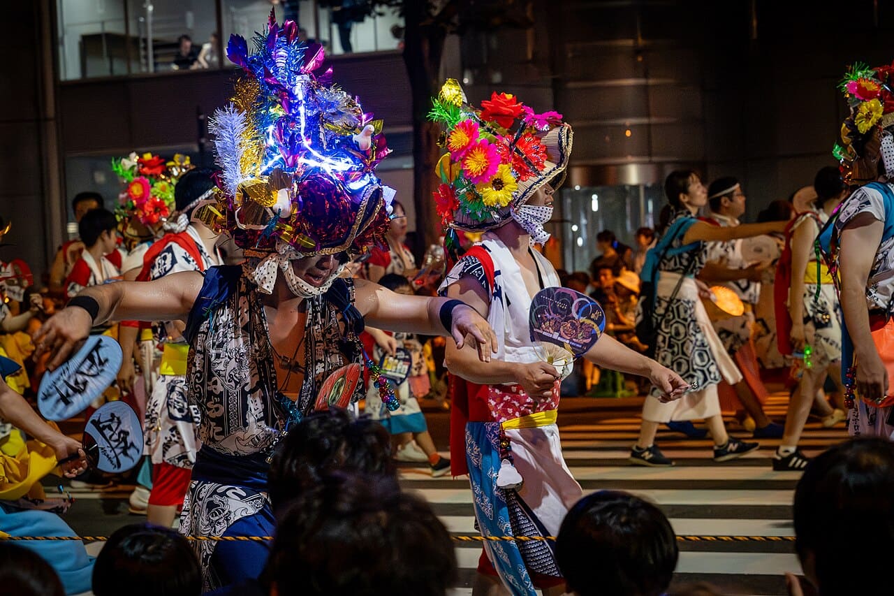 青森睡魔祭跳人隊伍，舞者頭戴綴滿花飾的花笠、身穿浴衣正裝在夜間街道上起舞