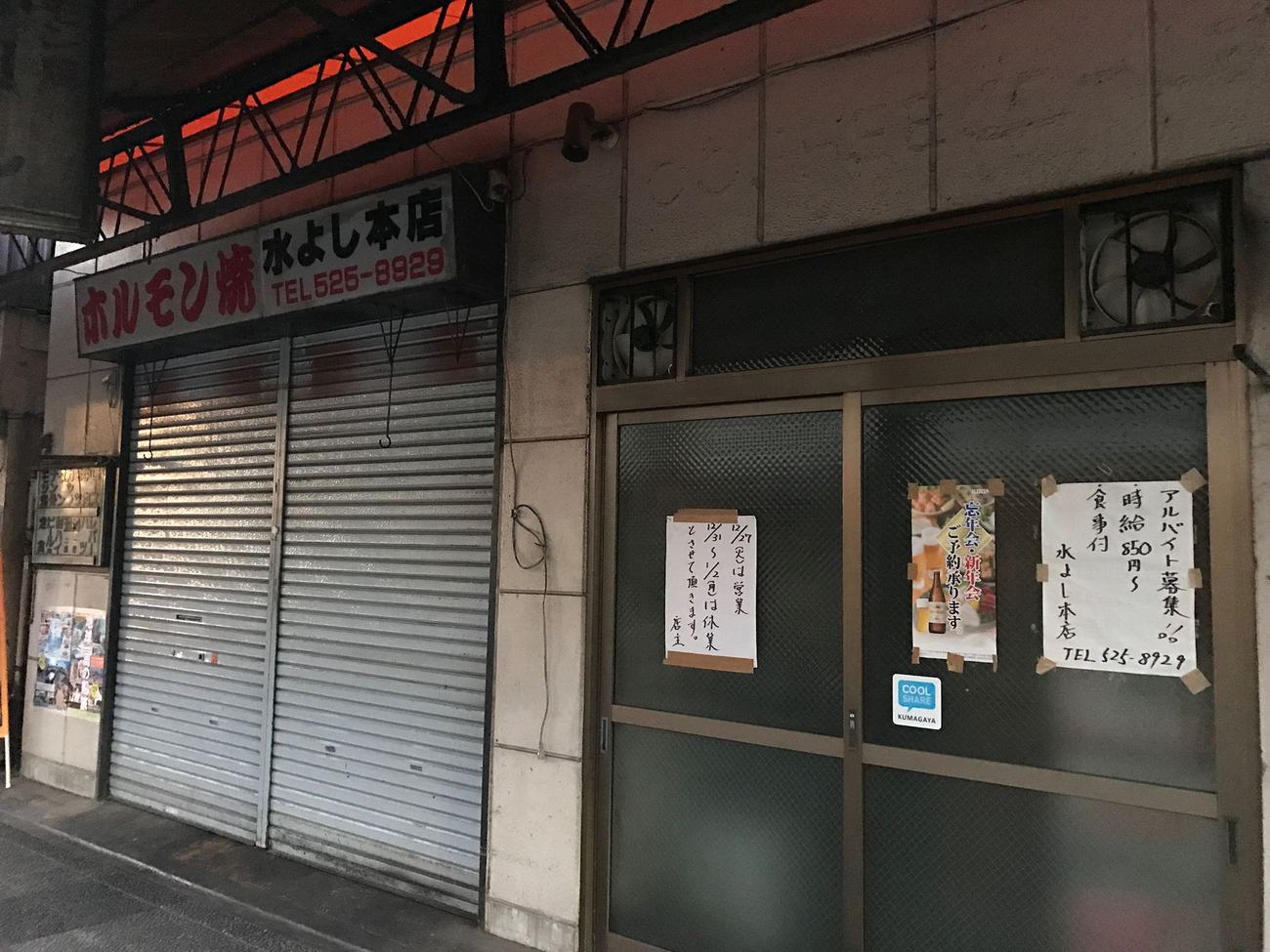 A Japanese independent restaurant with its shutter down and a handwritten year-end closure notice taped to the door, listing which days it is shut and when it reopens