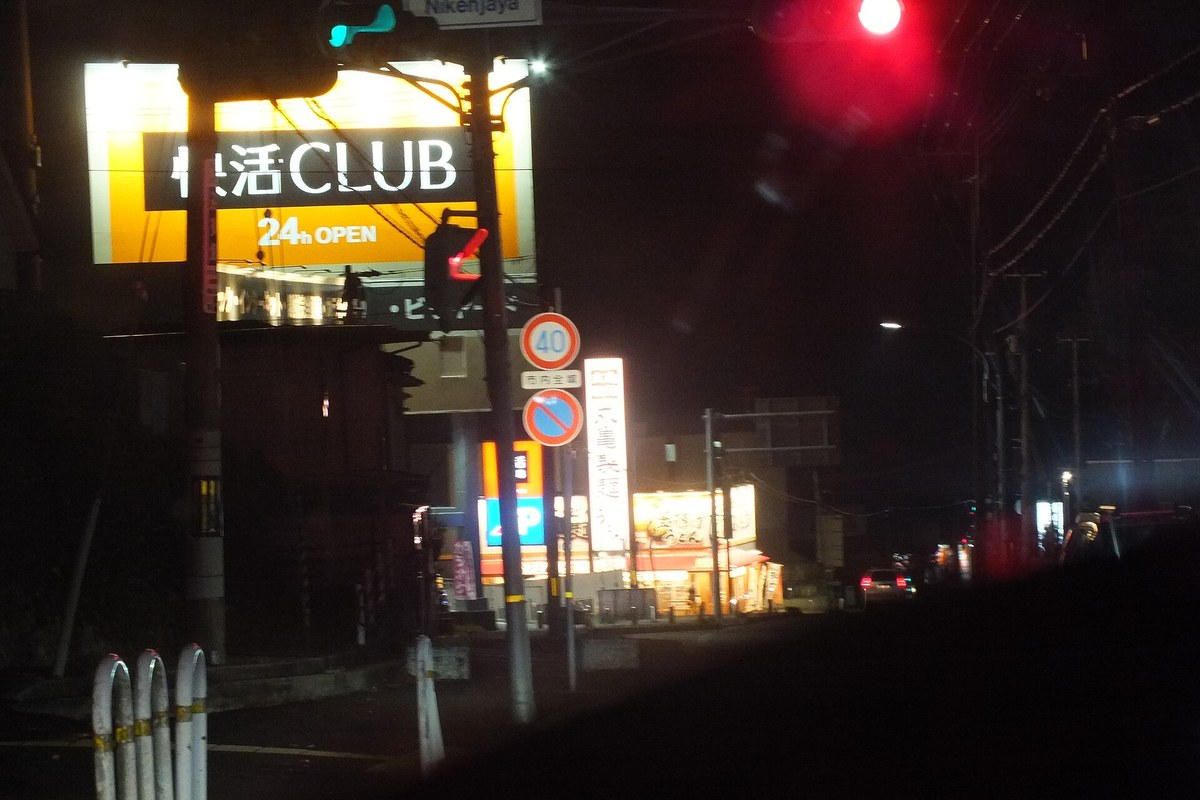 The illuminated roadside sign of a Kaikatsu Club internet cafe in Japan at night, marked 24h OPEN