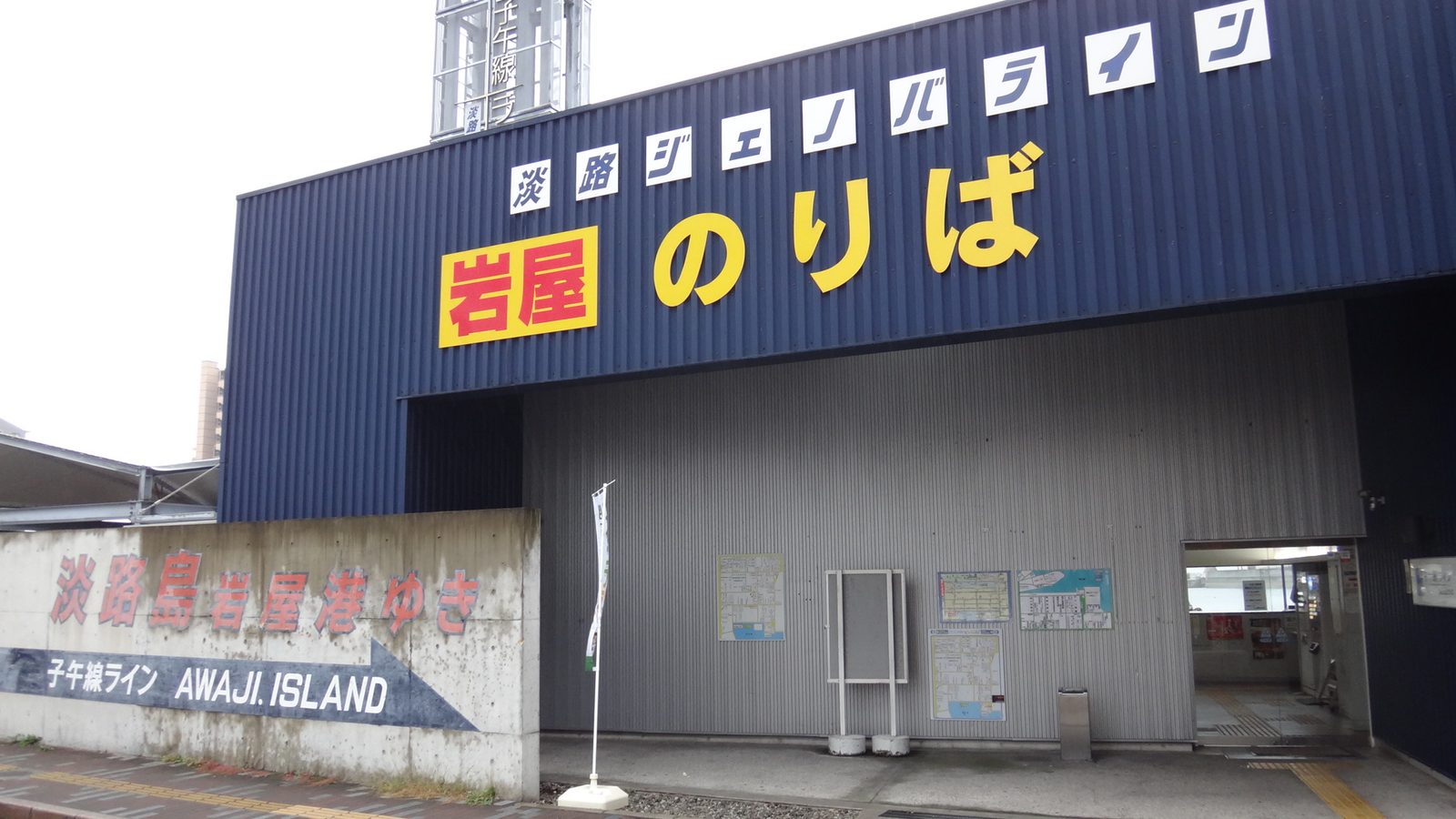 明石港的淡路ジェノバライン乘船處:深藍色建物正面寫著黃色大字「岩屋 のりば」,上方一排白底字是「淡路ジェノバライン」,左邊矮牆寫著淡路島岩屋港ゆき與 AWAJI ISLAND