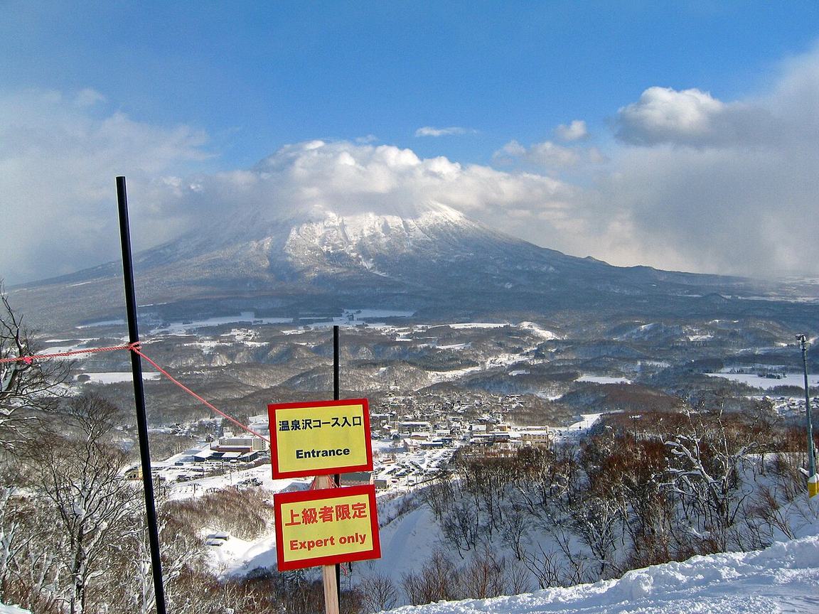 二世谷グラン・ヒラフ雪場的紅色境界繩與雙語告示牌「温泉沢コース入口 Entrance／上級者限定 Expert only」，背景是雲罩頂的羊蹄山