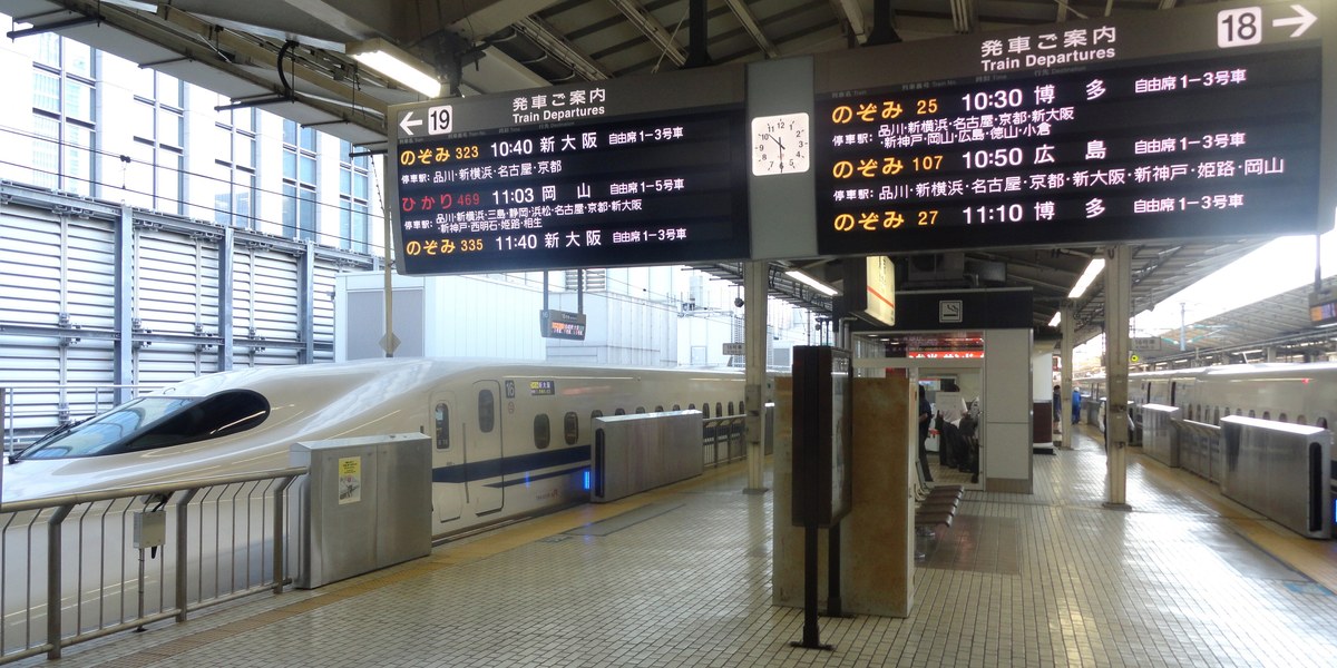 A Nozomi waiting at a Tokaido Shinkansen platform at Tokyo Station, the departure boards listing “non-reserved cars 1–3” beside every service