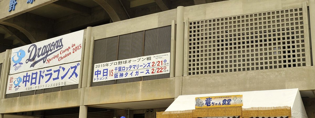 北谷公園野球場外牆掛的布條:左邊是「Dragons Spring Camp in Chatan 2015」與「歓迎 中日ドラゴンズ」,中間是「2015年プロ野球オープン戦 中日 VS 千葉ロッテマリーンズ 2/21(土)・阪神タイガース 2/22(日)午後1時」,右下是賣吃的帳篷「竜ちゃん食堂」