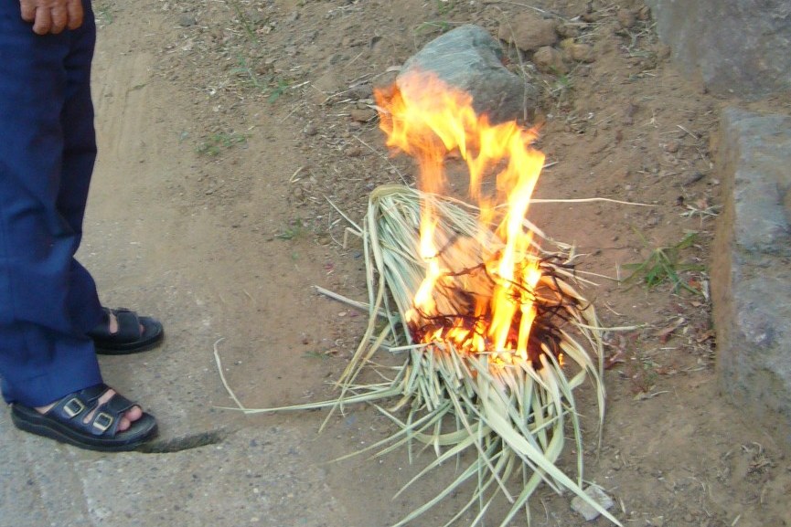 A mukaebi welcoming fire, a small bundle of hemp reeds burning on the ground at a Japanese house entrance at dusk, its light falling on the stone step