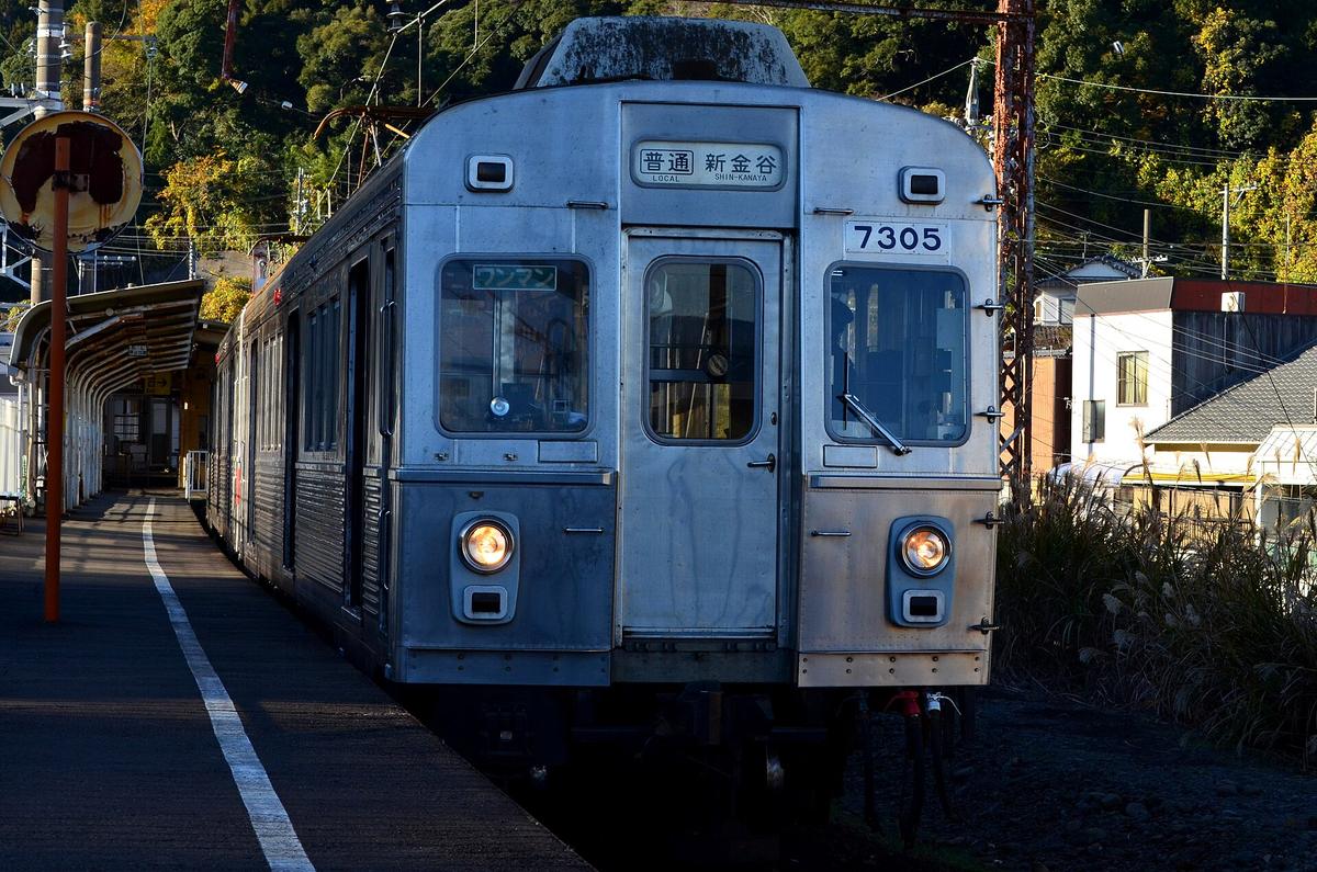 停在金谷站月台邊的大井川鐵道銀色不鏽鋼電車，車頭編號 7305，方向幕寫著「普通 新金谷 LOCAL SHIN-KANAYA」，兩盞頭燈亮著
