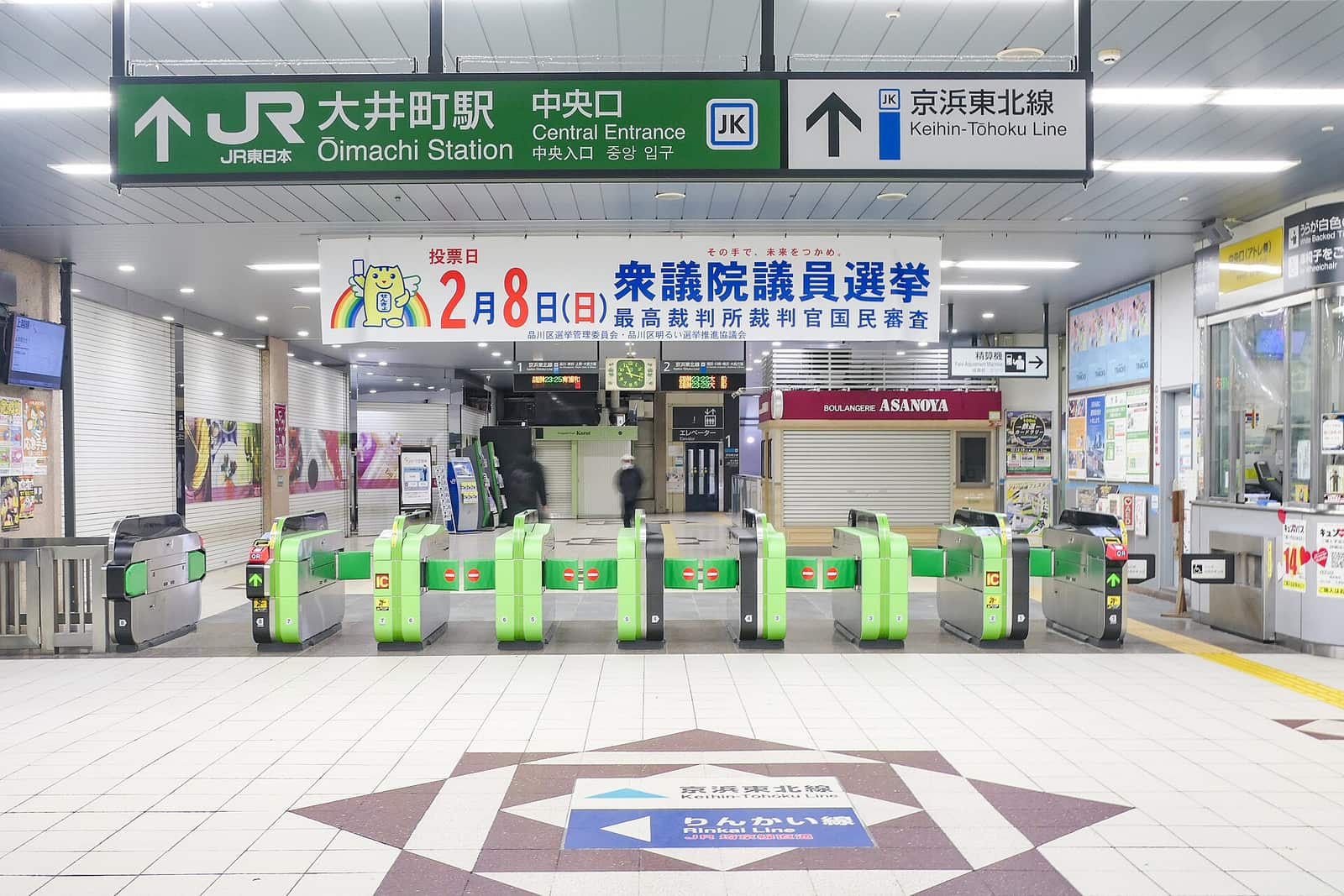 A row of green automatic ticket gates at the Central Entrance of JR Oimachi Station, under a green overhead sign reading Oimachi Station Central Entrance and a blue one reading Keihin-Tohoku Line, with orange IC card readers on the side of each gate and floor arrows separating the Keihin-Tohoku and Rinkai lines